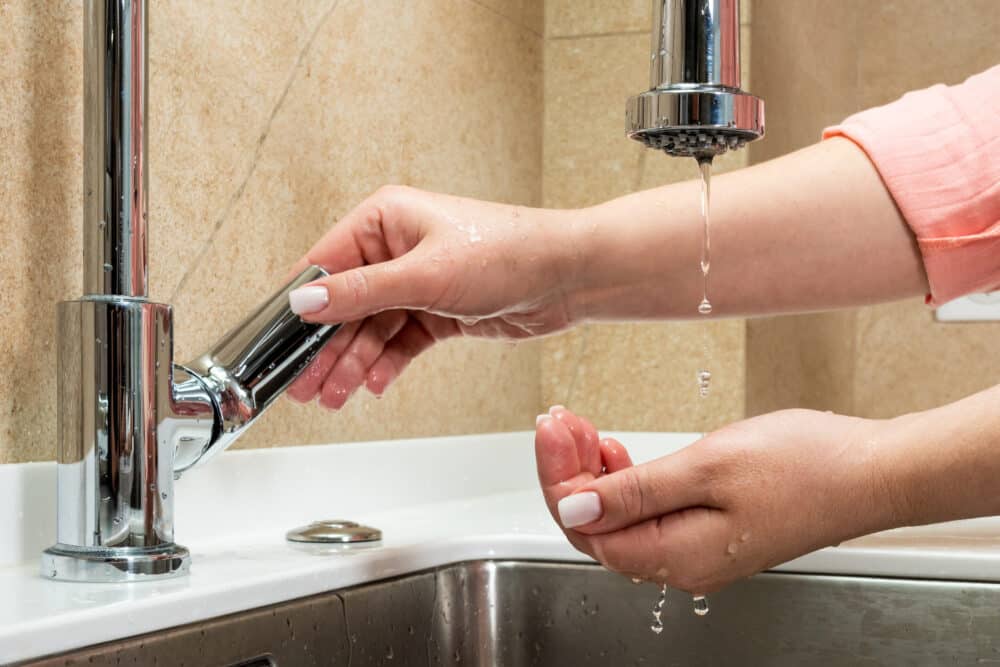 Woman turning on sink faucet to rinse hands under a trickle of water before increased water pressure,
